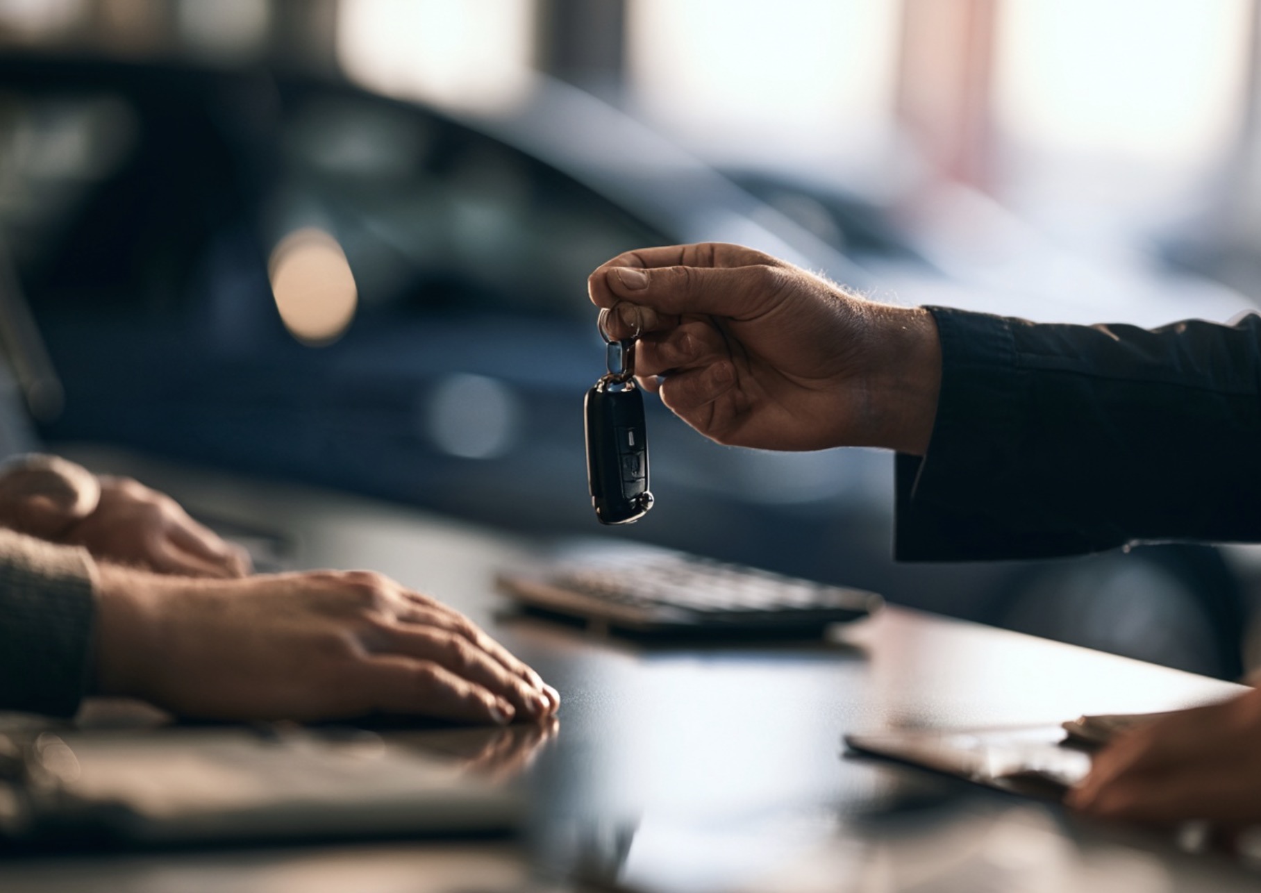 Hand geeft een autosleutel aan een andere hand boven een tafel
